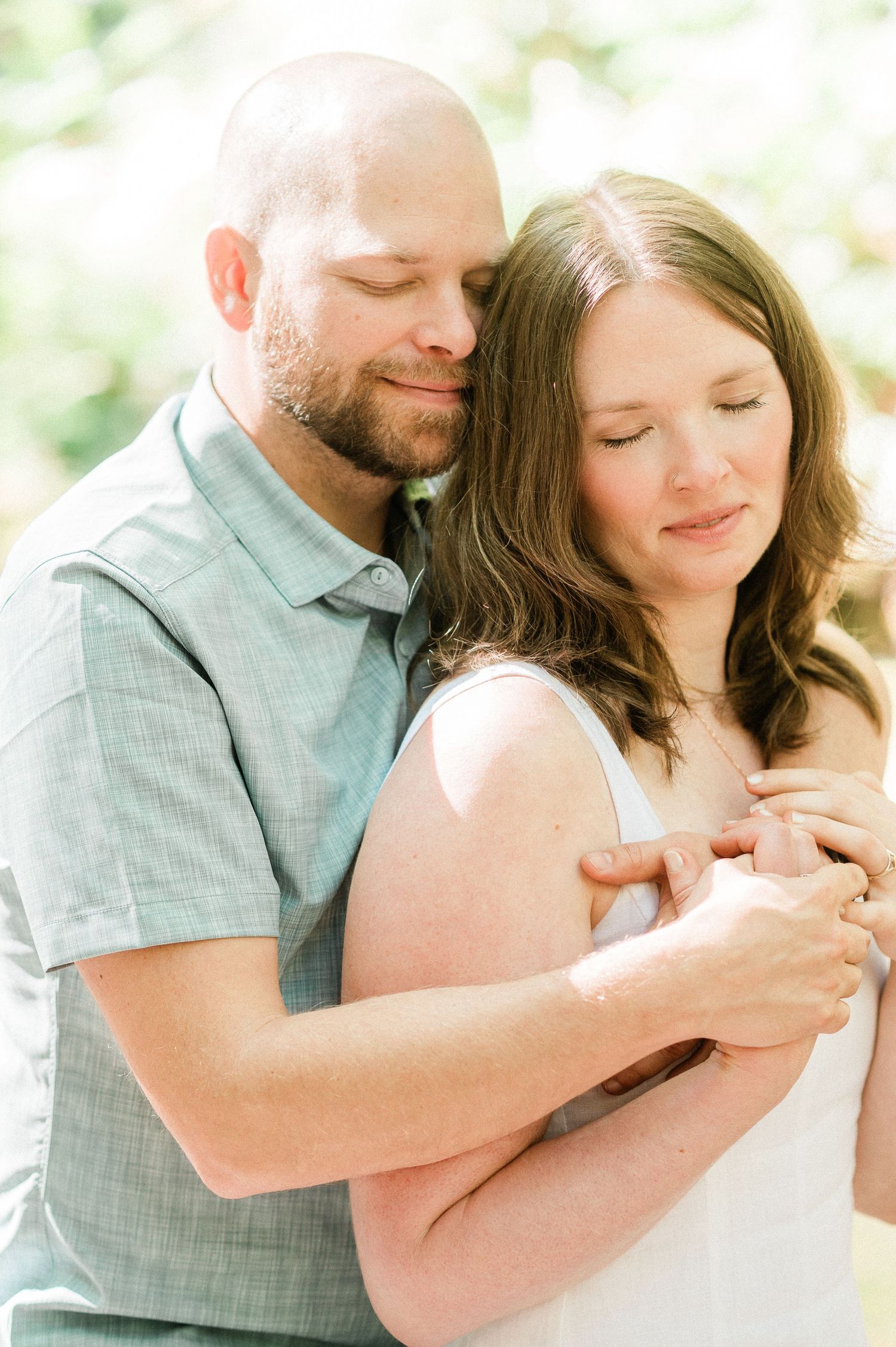 A tender embrace captured in soft natural light shows a couple sharing an intimate moment outdoors.