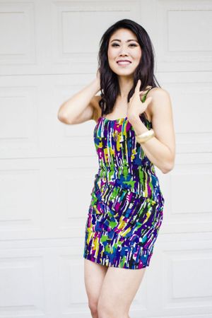 Woman in colorful patterned mini dress poses playfully against white background.