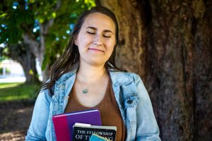 Person relaxing against tree trunk while holding a book outdoors.