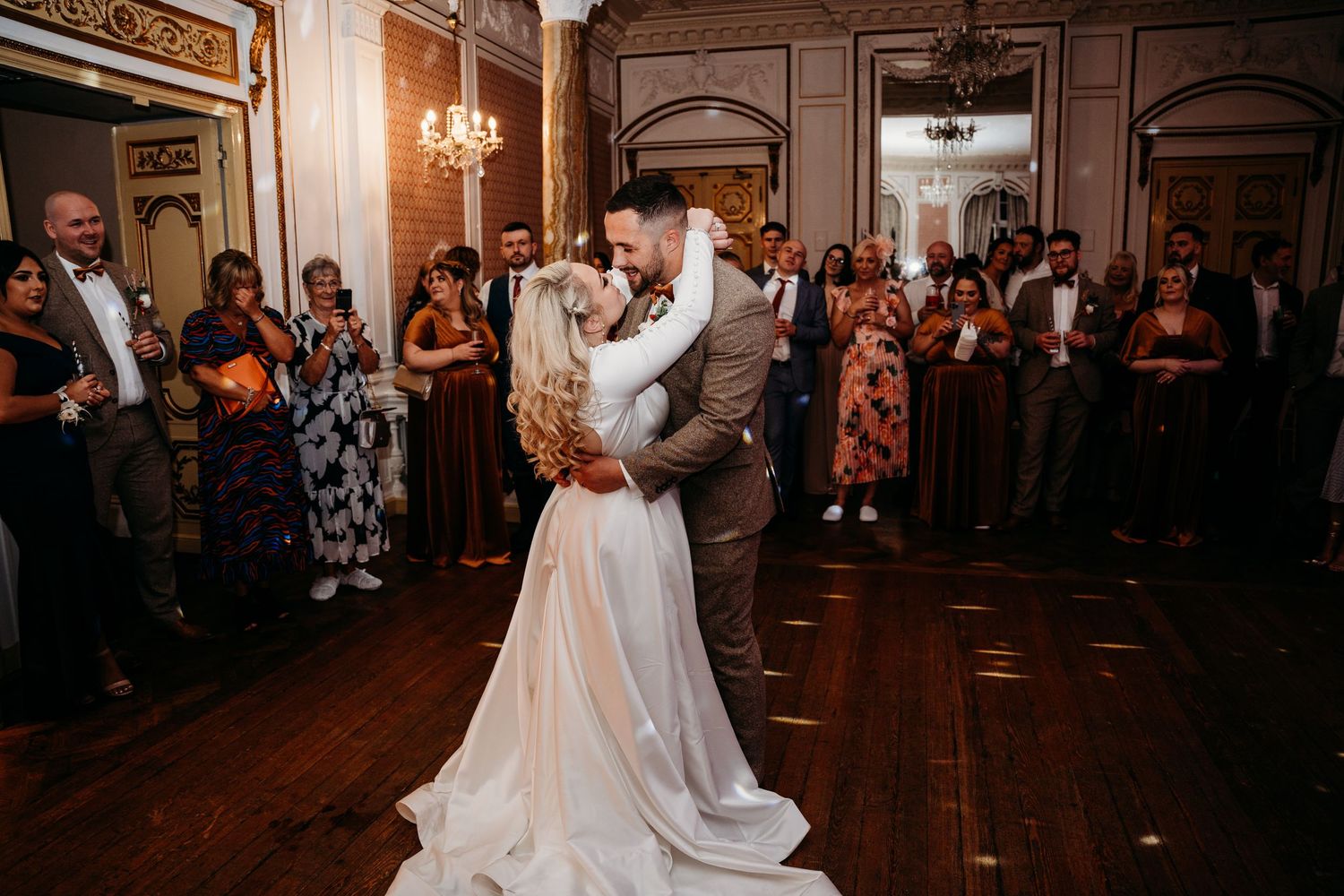 A couple shares their first dance at an elegant wedding reception while guests watch from the sidelines.