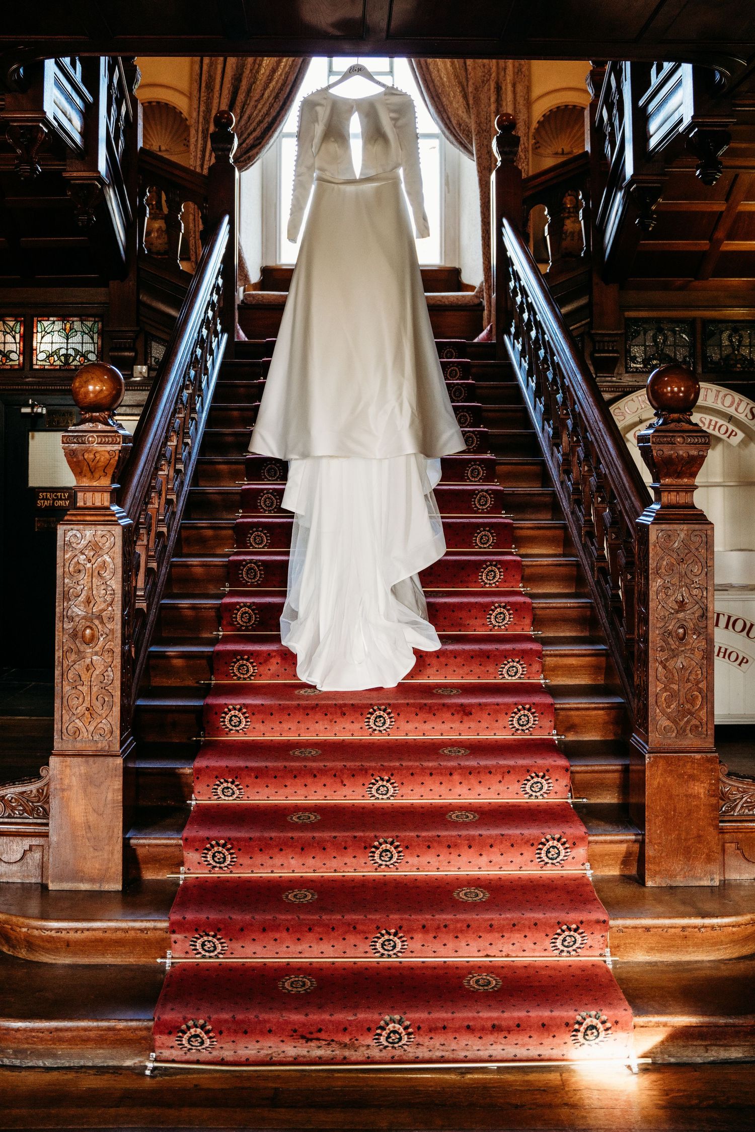 Classic white wedding gown displayed on grand staircase with red carpet and ornate wooden banisters.