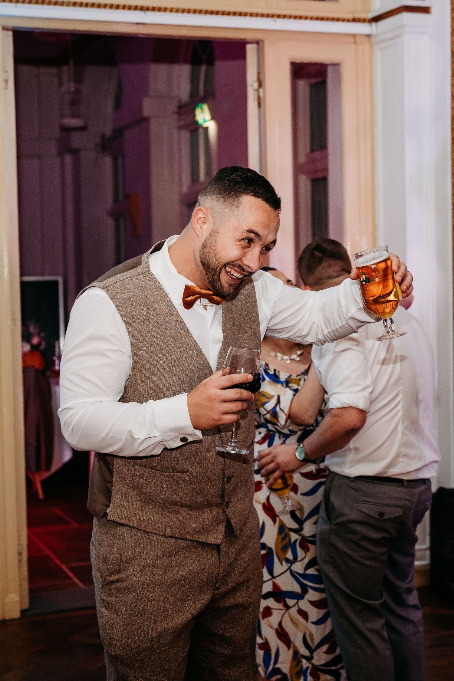 A guest in a brown tweed vest enjoys a drink during the wedding reception.
