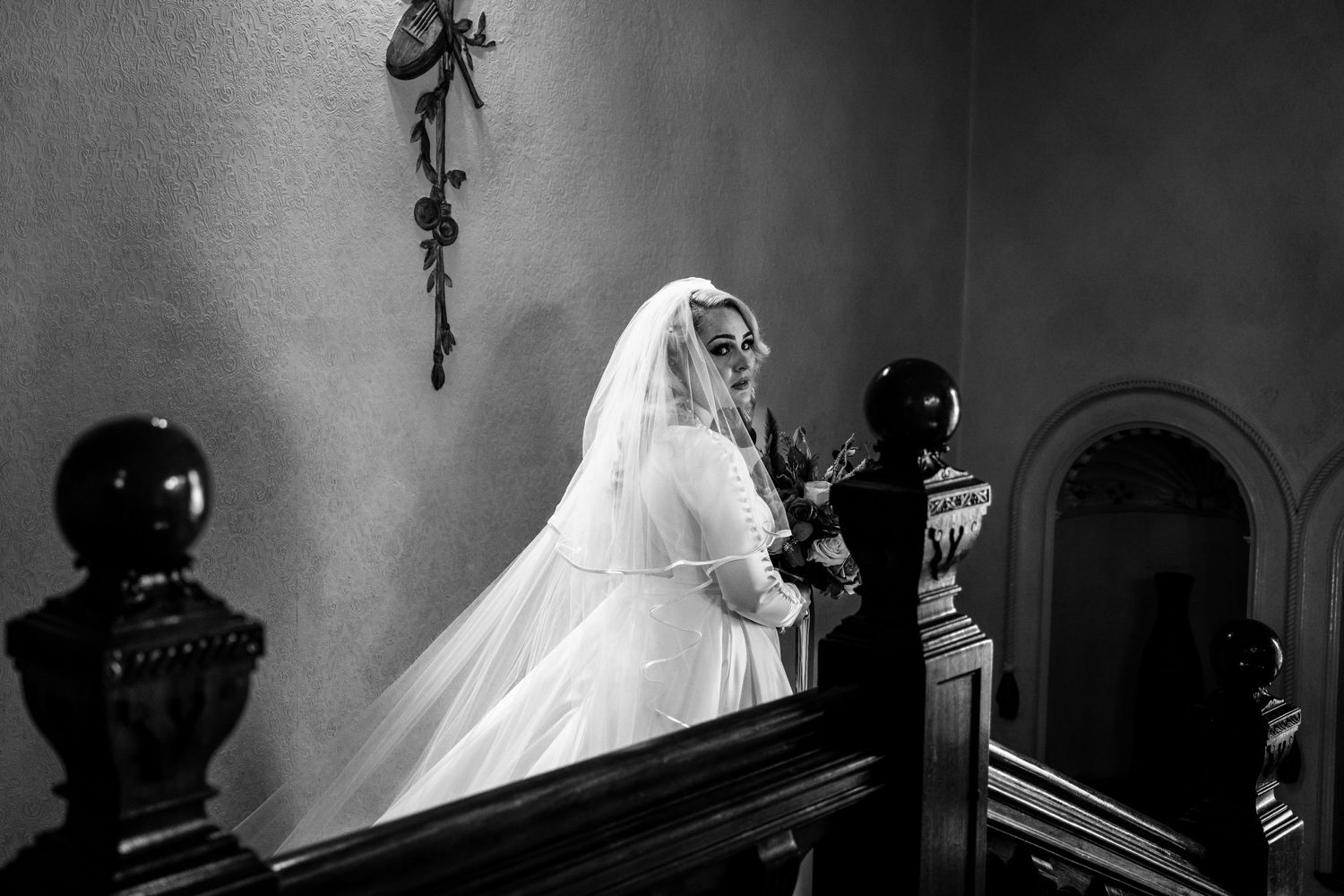 A dramatic black and white photo of someone ascending a grand staircase in a wedding gown.