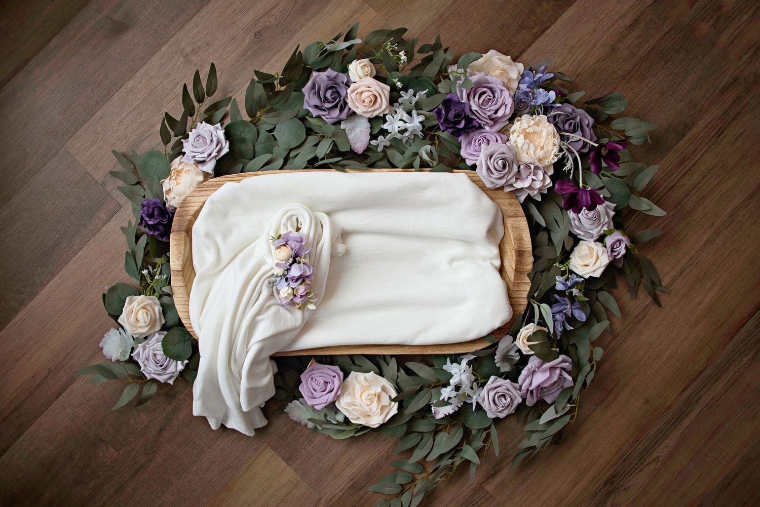 Newborn photography setup with floral wreath arrangement in purple and white.