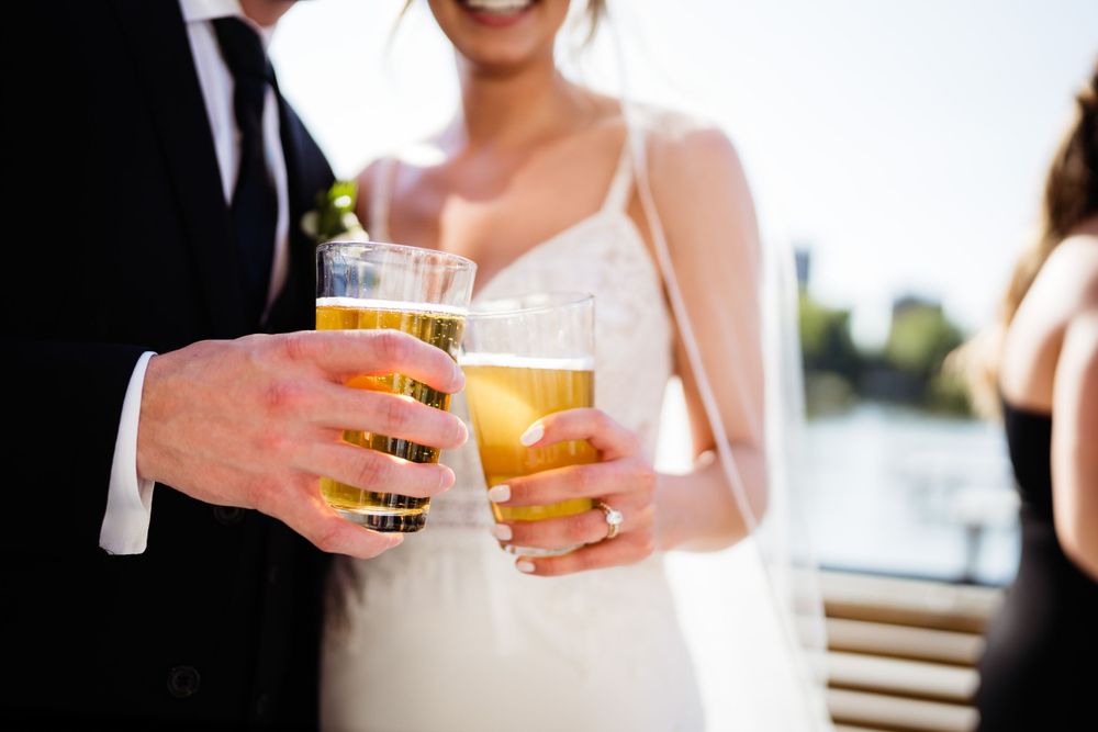 Wedding couple toasts with craft beers in outdoor setting.