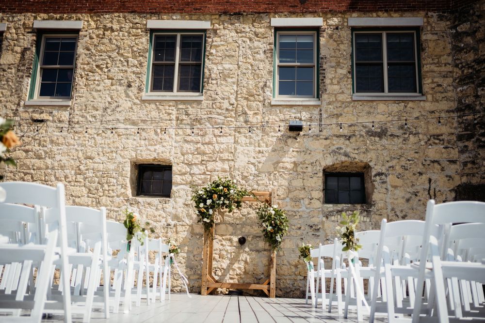 Outdoor wedding ceremony setup with white chairs against rustic stone wall.