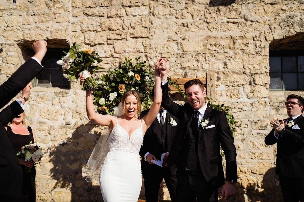 Newlyweds celebrate joyfully under floral arch during outdoor ceremony.