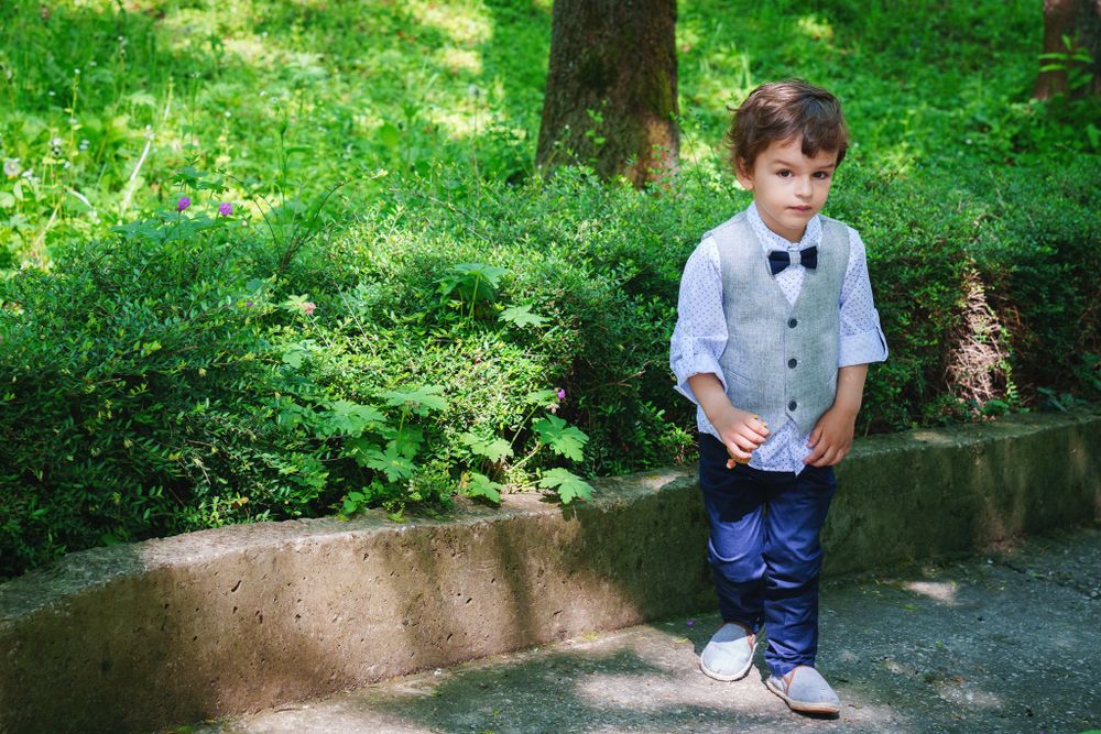 Young boy in formal attire standing outdoors in a garden setting.