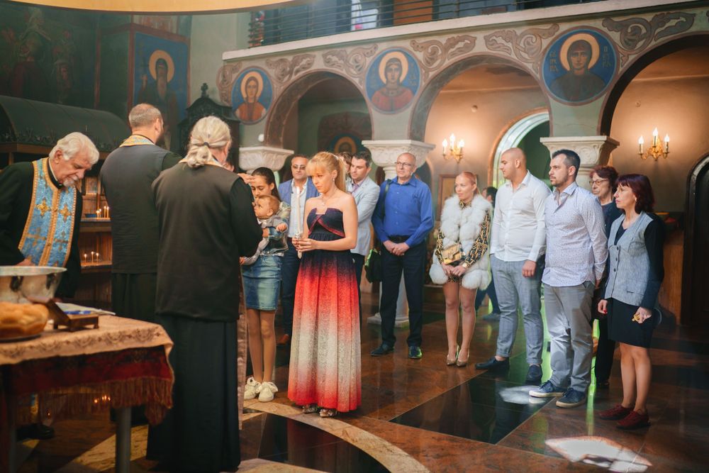 Orthodox priest conducting a ceremony with a group of people gathered in a decorated church.