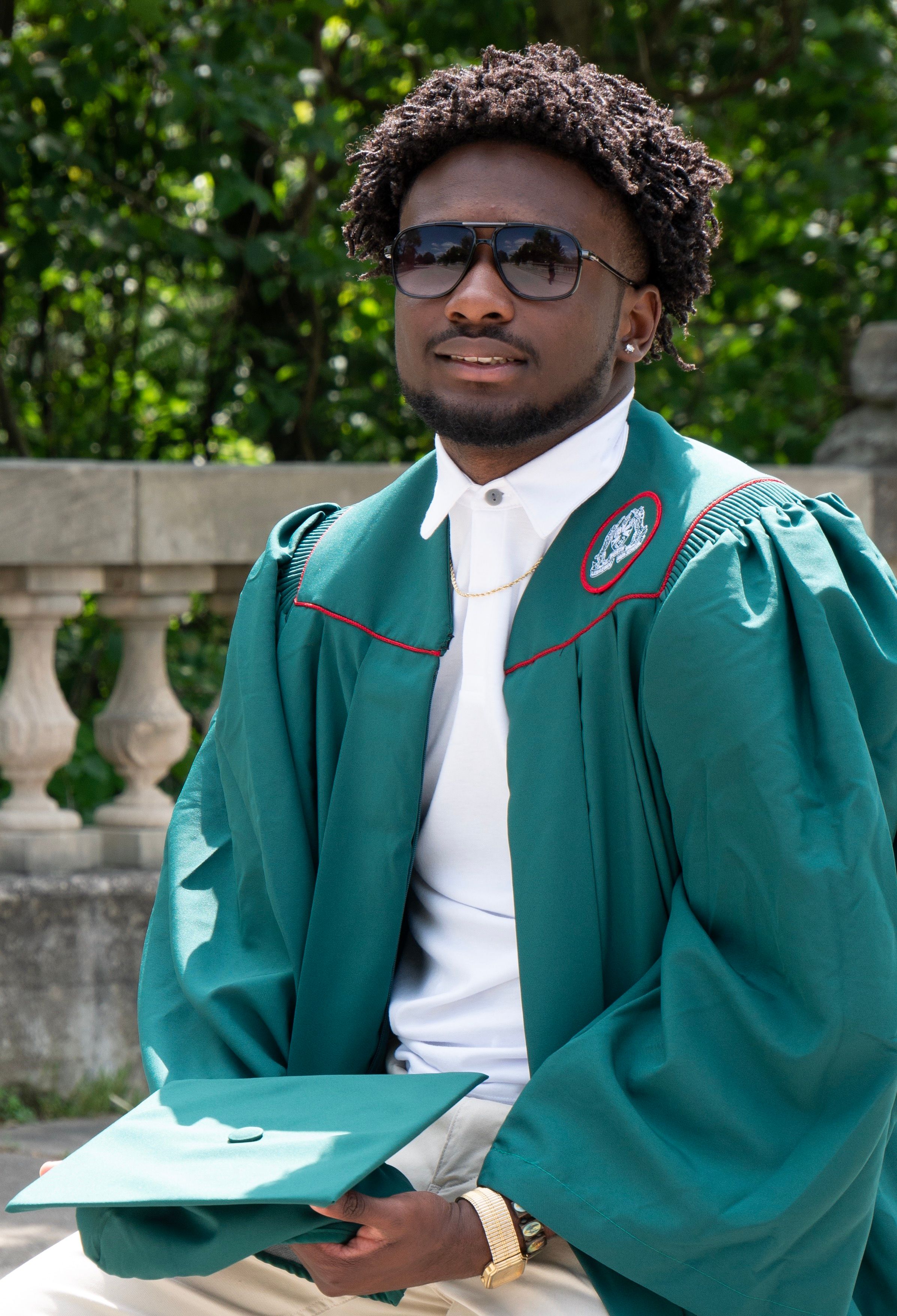 Graduate in emerald green academic regalia holding diploma outdoors.