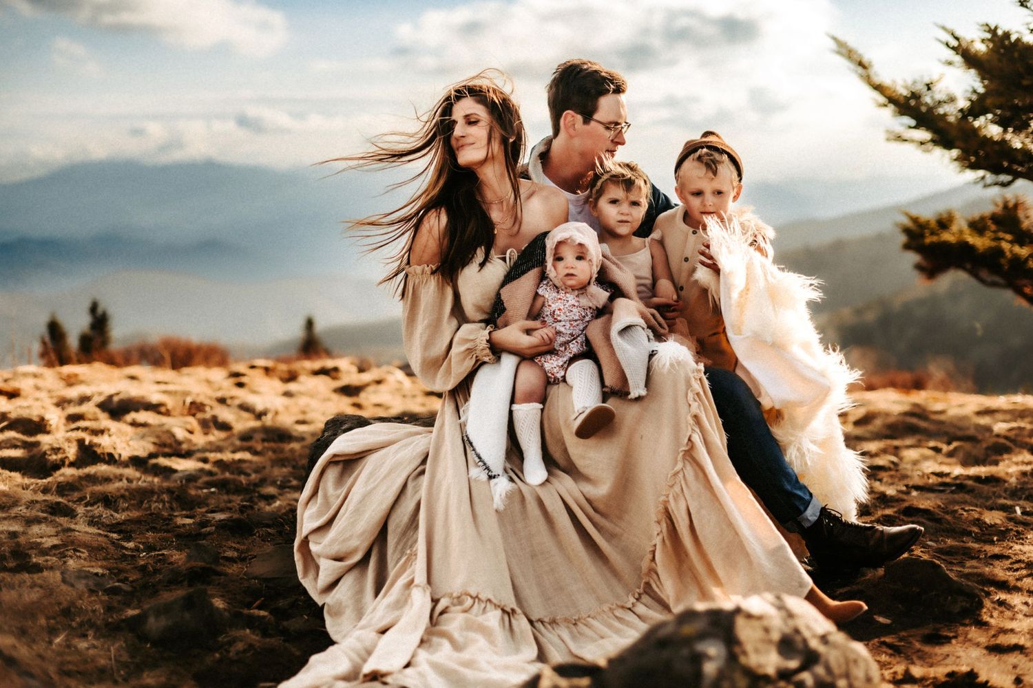 Joyful family moment captured on a mountaintop with flowing dresses and dramatic mountain backdrop.