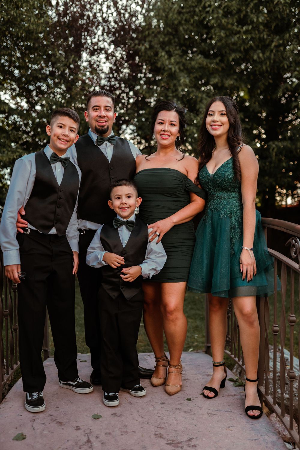 Elegant family of five in formal attire posing on a bridge at sunset.