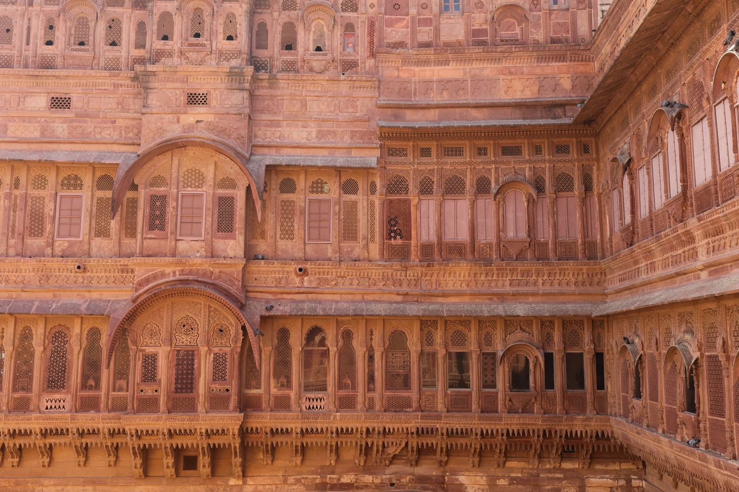 Sandstone courtyard with ornate archways and balconies in traditional Rajasthani architecture.