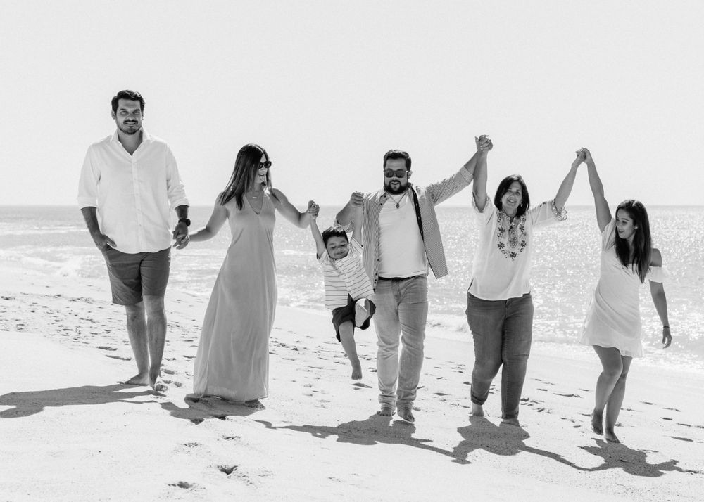 A joyful group walking together hand-in-hand along a sunny beach in casual white outfits.