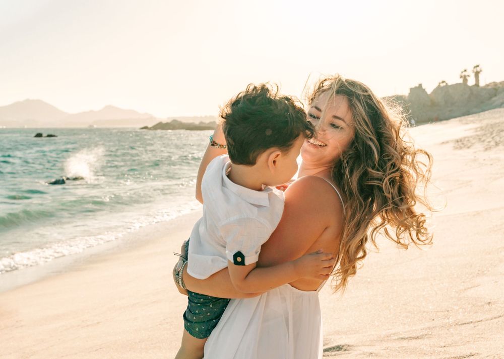 A candid moment of joy and laughter on a sunny beach with ocean waves in the background.