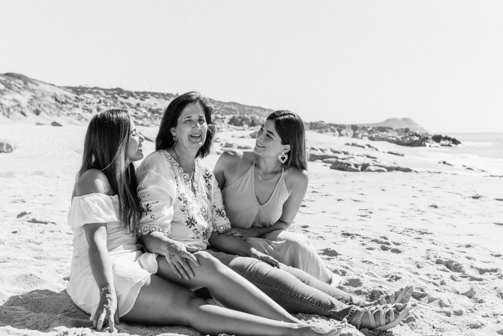Three people sitting and laughing together on sandy beach in black and white.