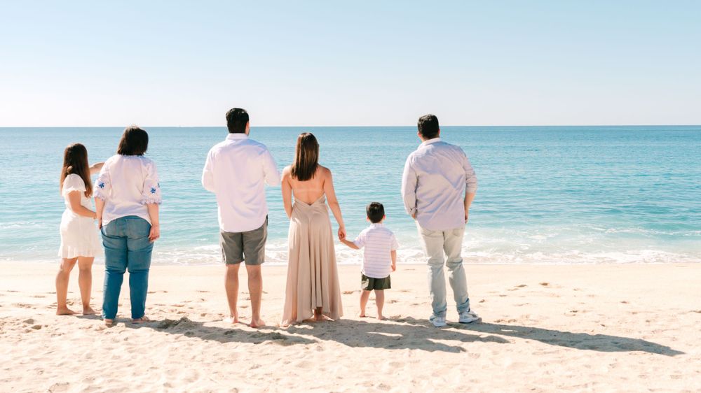 Family standing together looking at ocean view on sandy beach.