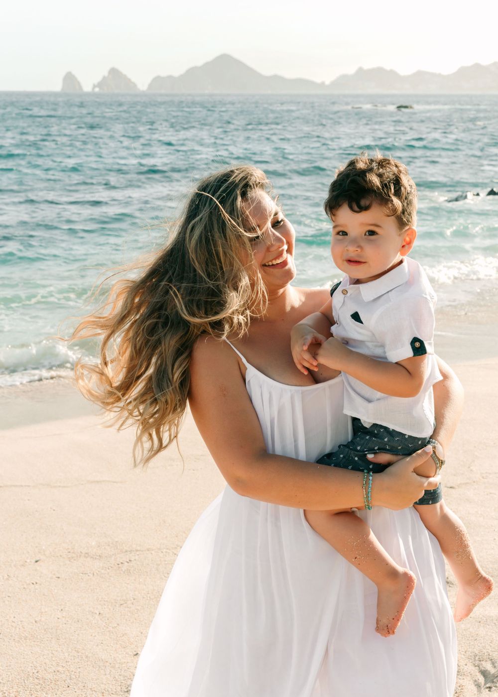 A tender beachside moment with mountains visible across the crystal blue waters.