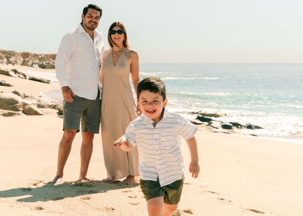 Candid beach family photo with child running joyfully in foreground.