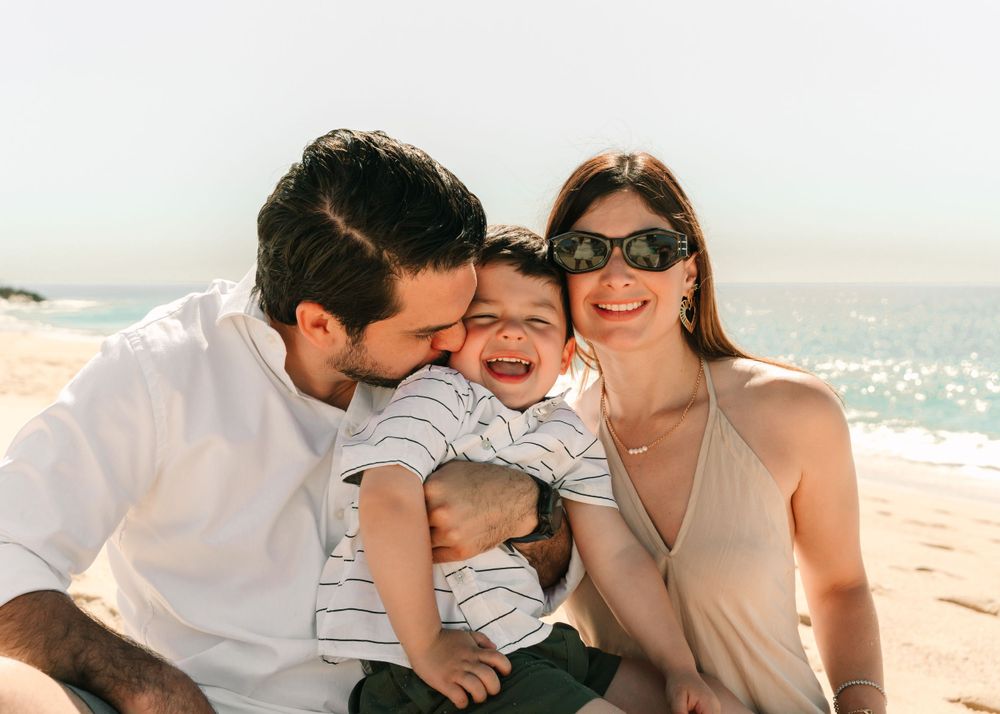 A happy family moment captured on a sunny beach with ocean waves in the background.
