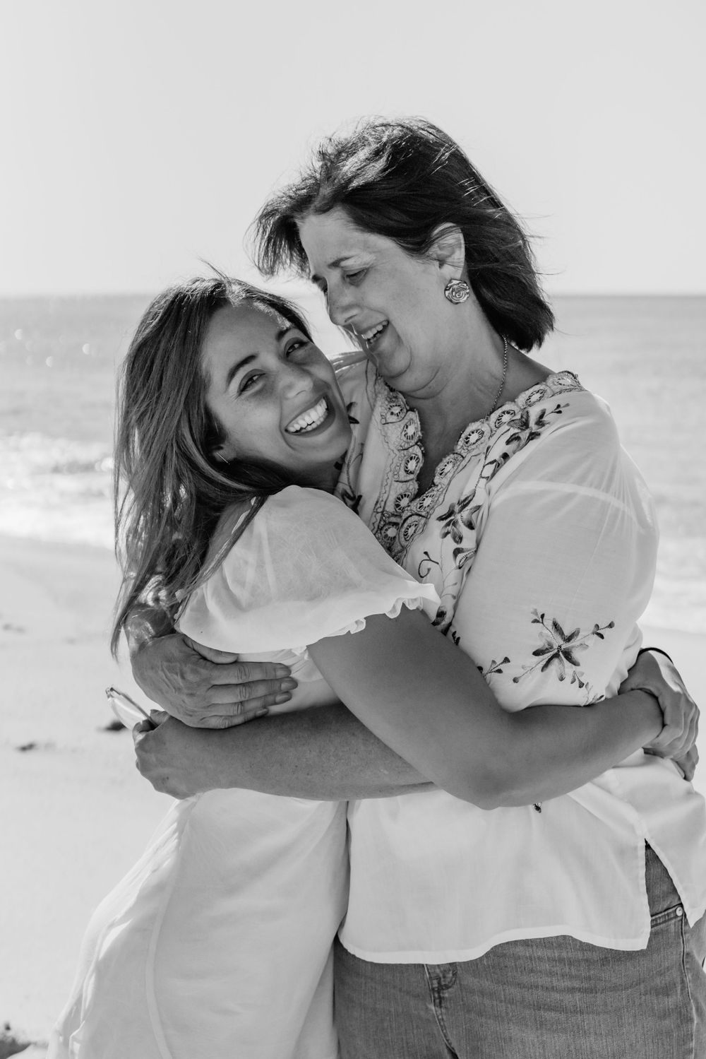 Heartwarming black and white photo of mother and daughter embracing on beach.