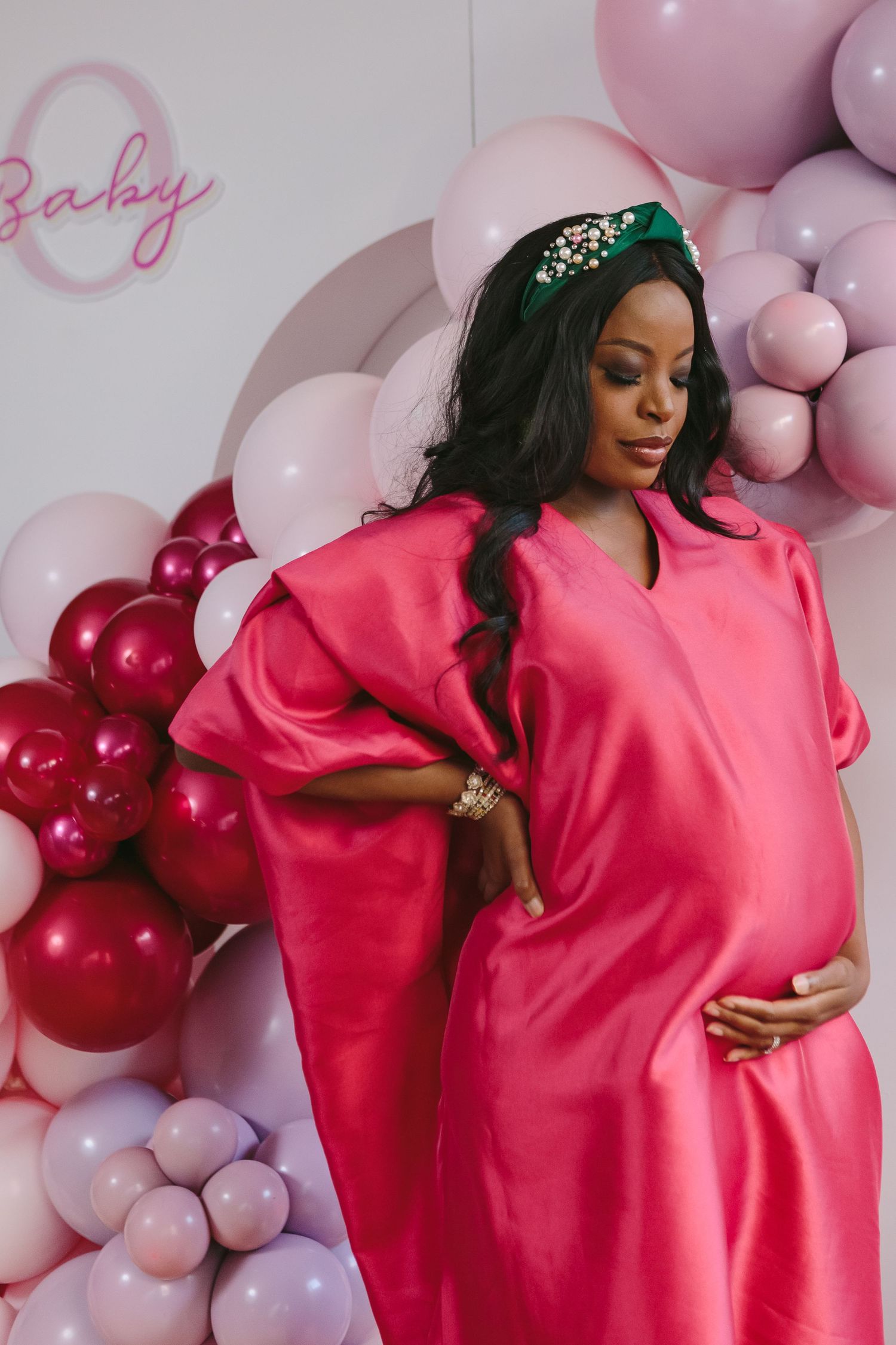 a pregnant mother wearing bright pink standing next to a balloon arch on her baby shower photographed by Paula Ortiz NY