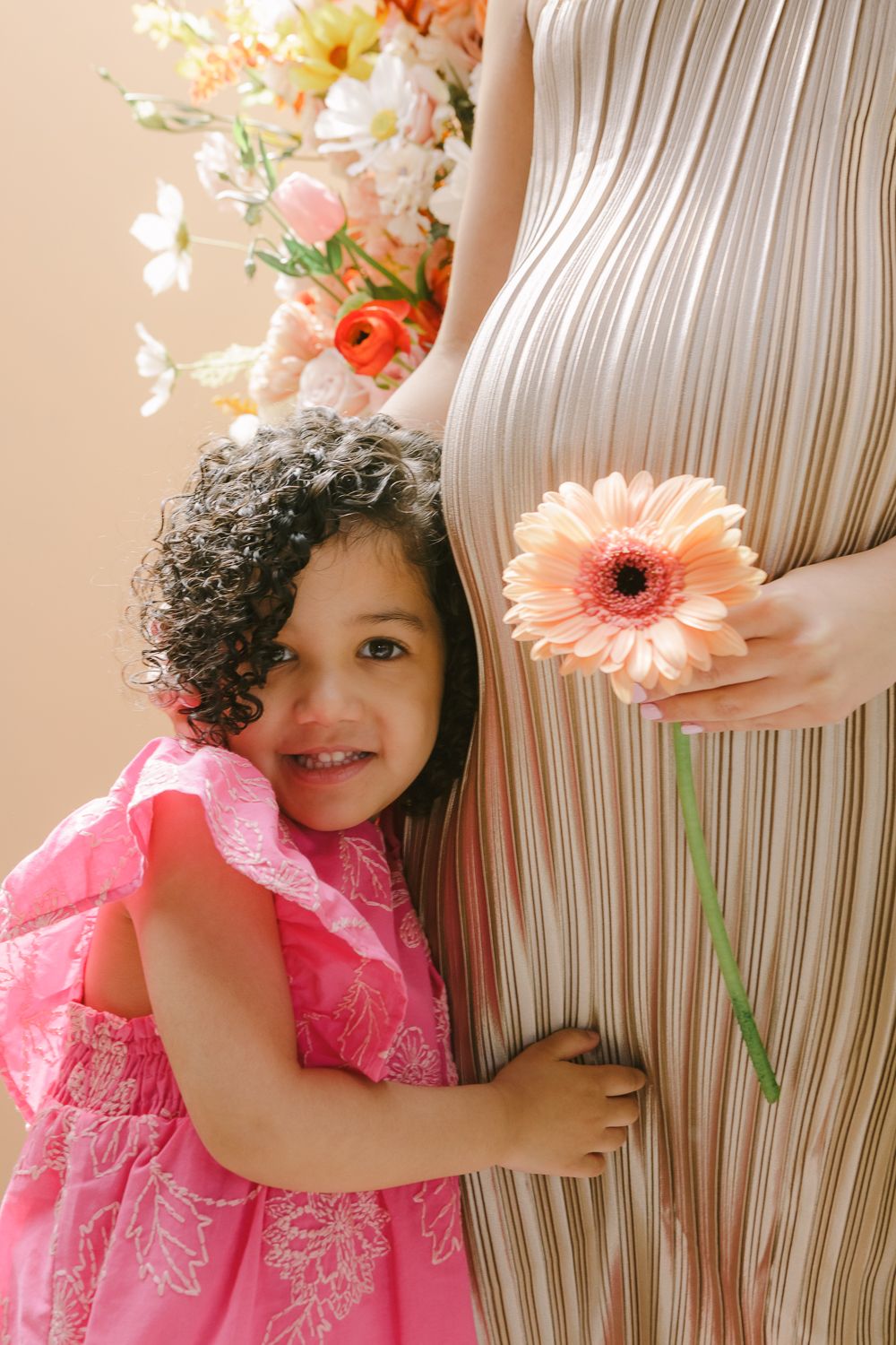 a close up view of a toddler girl in a pink dress hugging her mom's pregnant belly, photo by NYC family photographer