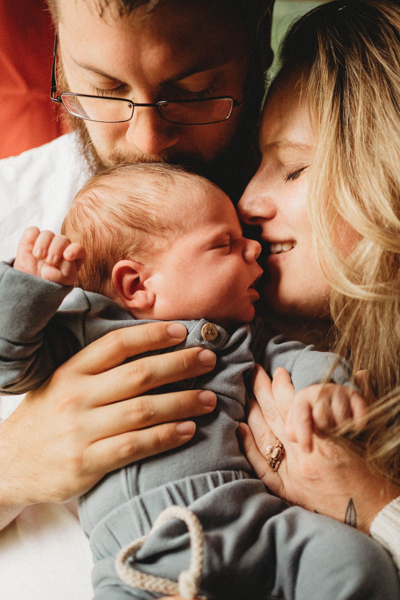 Tender moment with newborn baby being cradled and kissed by parents.
