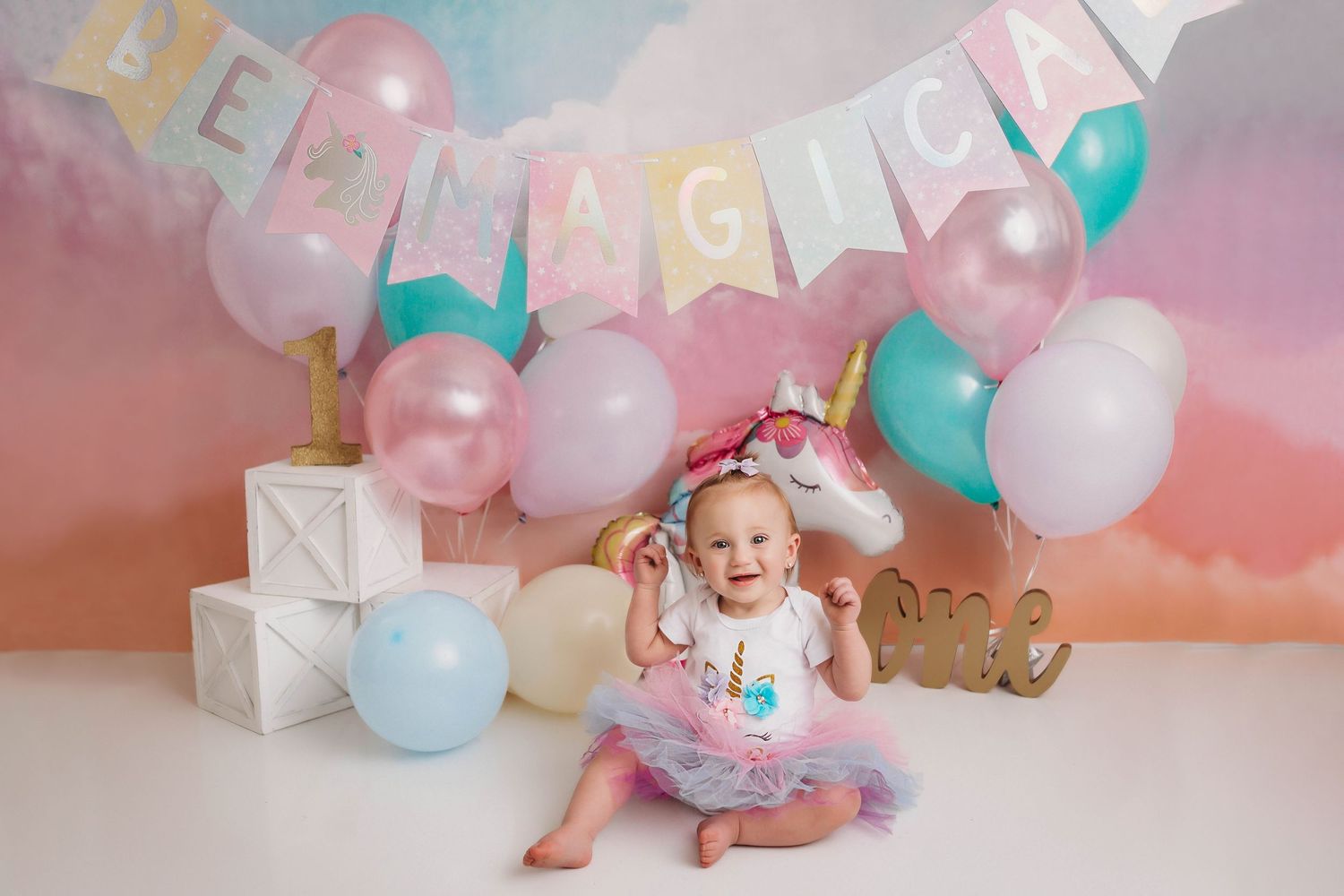 Baby celebration setup with pastel balloons and 'BE MAGICAL' banner against pink backdrop.