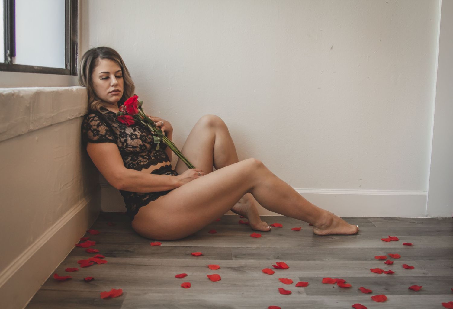 Person lounging on floor with scattered rose petals in minimal room setting.