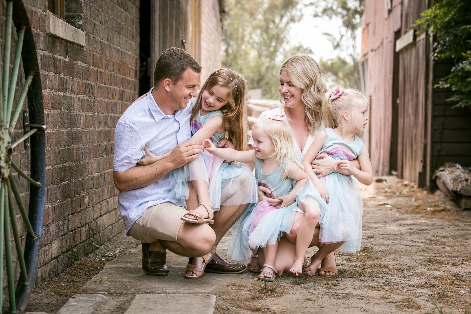 family portrait with three young girls tickling dad