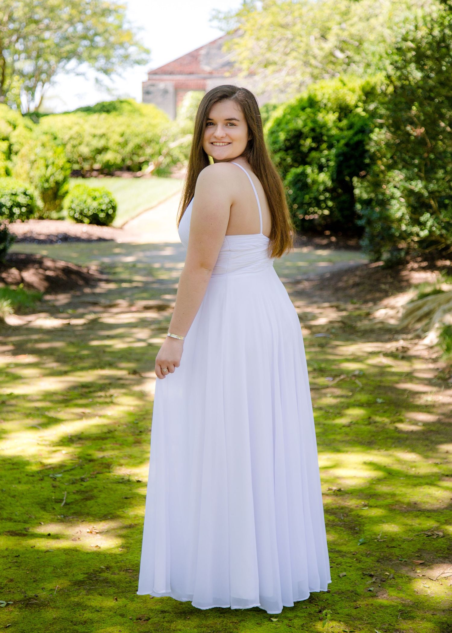 A young woman in a flowing white strapless gown poses in a lush garden setting.