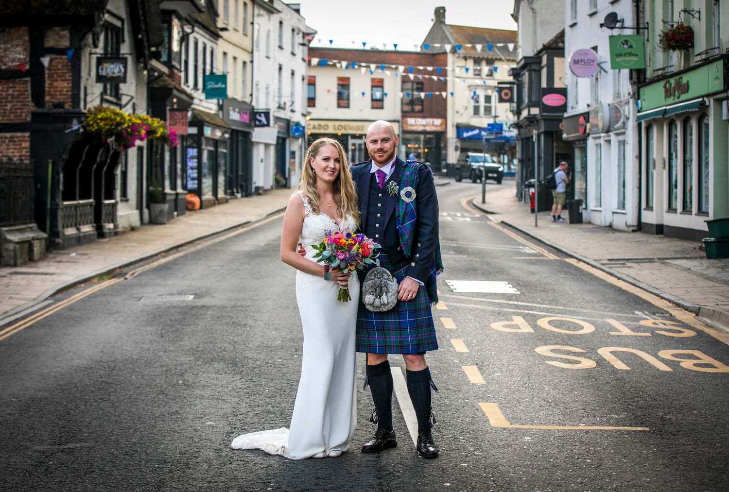 A couple walks together on a quaint cobblestone street with historic buildings in the background.