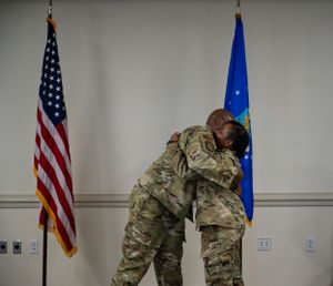 Two service members embrace during a military ceremony between U.S. and Air Force flags.