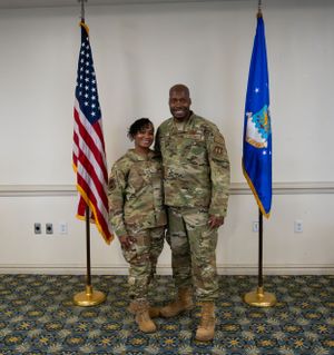 Two service members in camouflage uniforms pose for photo between American and Air Force flags.