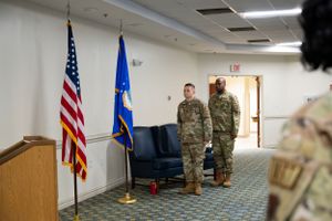 Service members standing at attention by flags during military ceremony.