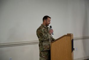 Service member delivers remarks at wooden podium during military ceremony.