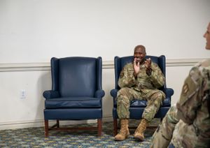 Service member seated in blue chair during formal military event.