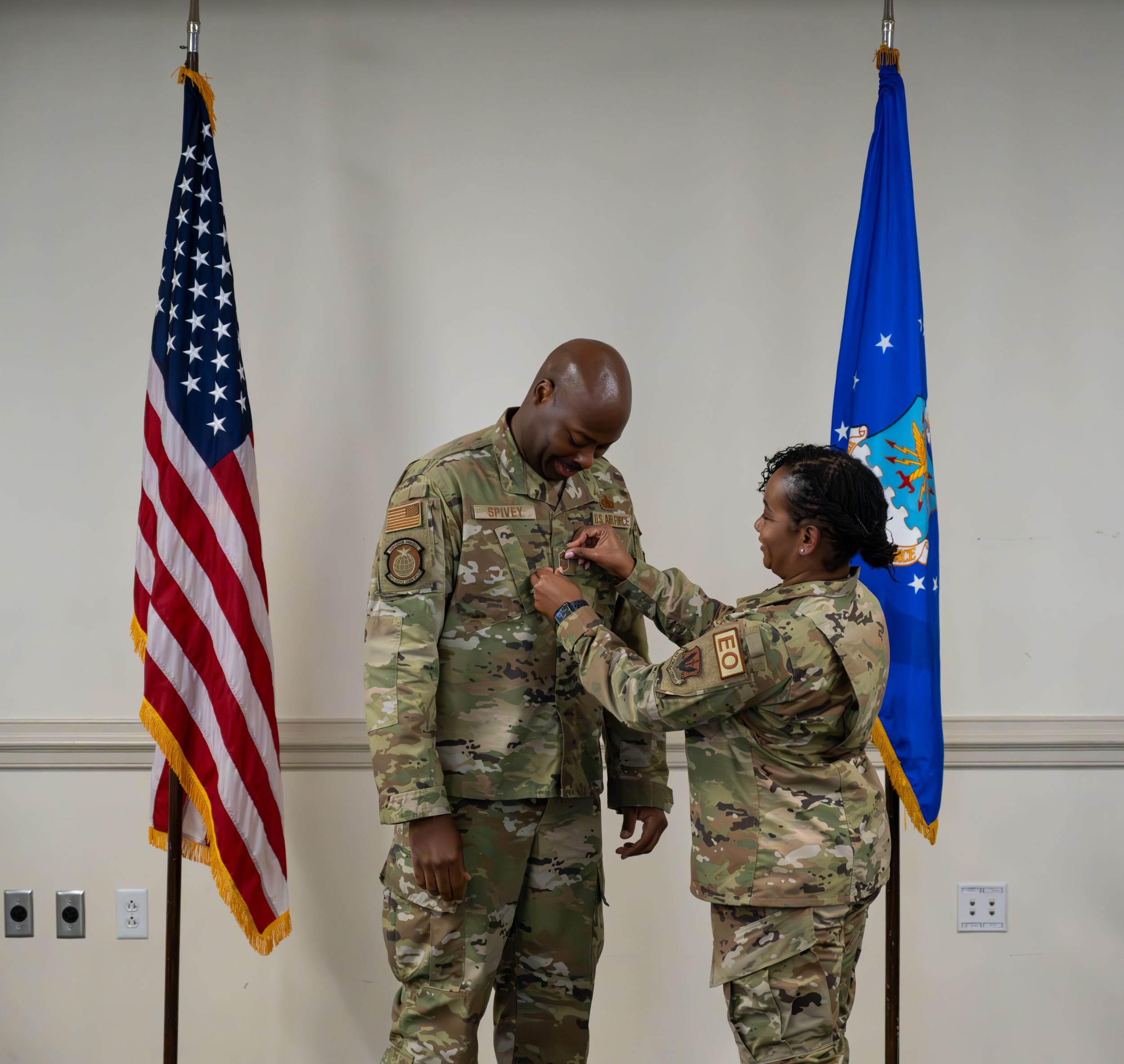 Promotion ceremony taking place between two service members with US and Air Force flags in background.