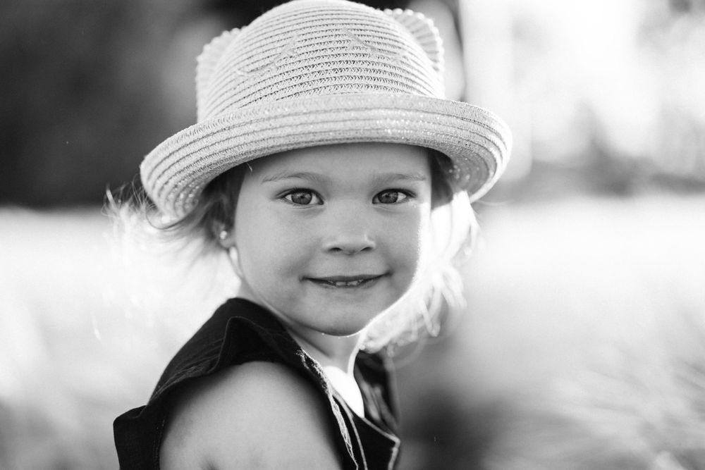 Sweet portrait of a child wearing a white sun hat against a bright background.