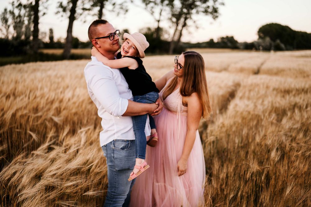 Loving family portrait in a golden wheat field during sunset.