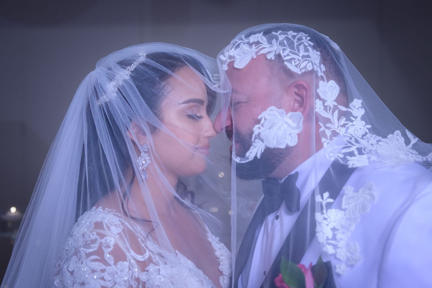 A romantic wedding moment captured through delicate lace veil as newlyweds share an intimate kiss.