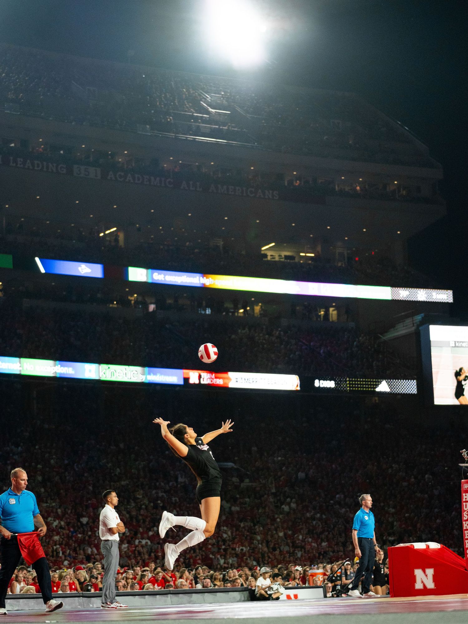 A volleyball player executes a spectacular jump serve during a match in a packed outdoor stadium.