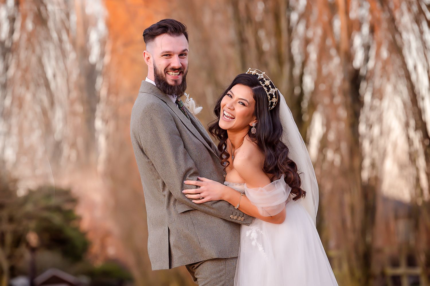 A couple embraces outdoors in their wedding attire against a backdrop of autumn trees.