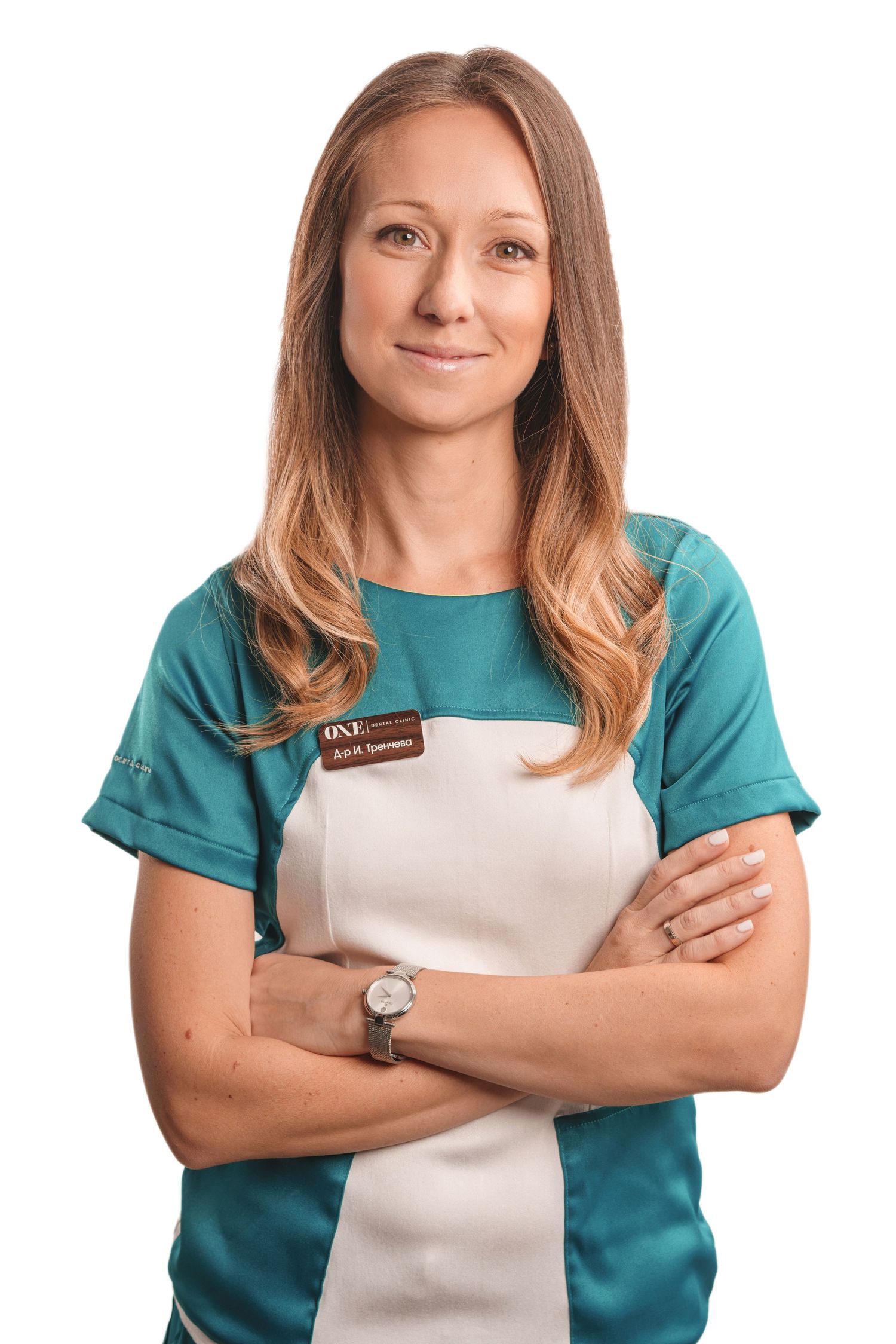 Healthcare worker in teal scrubs and white apron posing with crossed arms.