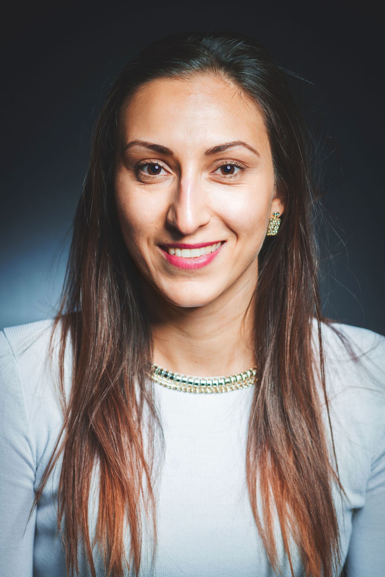 Studio portrait of a person wearing a white top with long dark hair against a dark background.