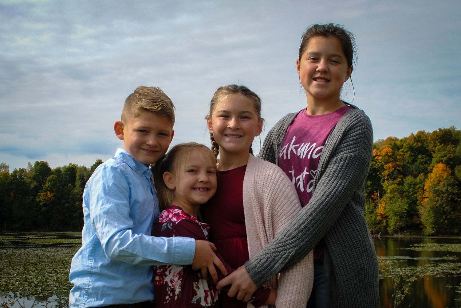 Group poses together for outdoor family photo near autumn lake with colorful foliage.
