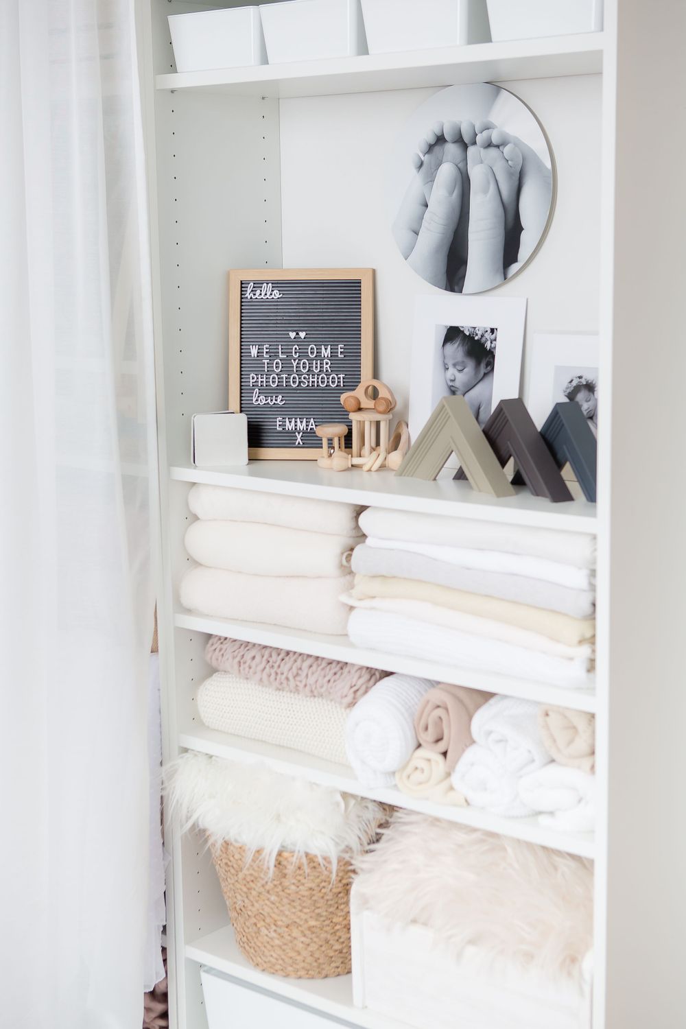 Clean white linen closet with letter board, decorative accents, and organized towels on shelves.