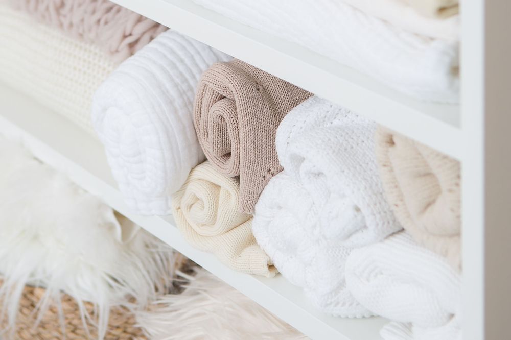 Neatly folded white and beige blankets arranged on storage shelf.