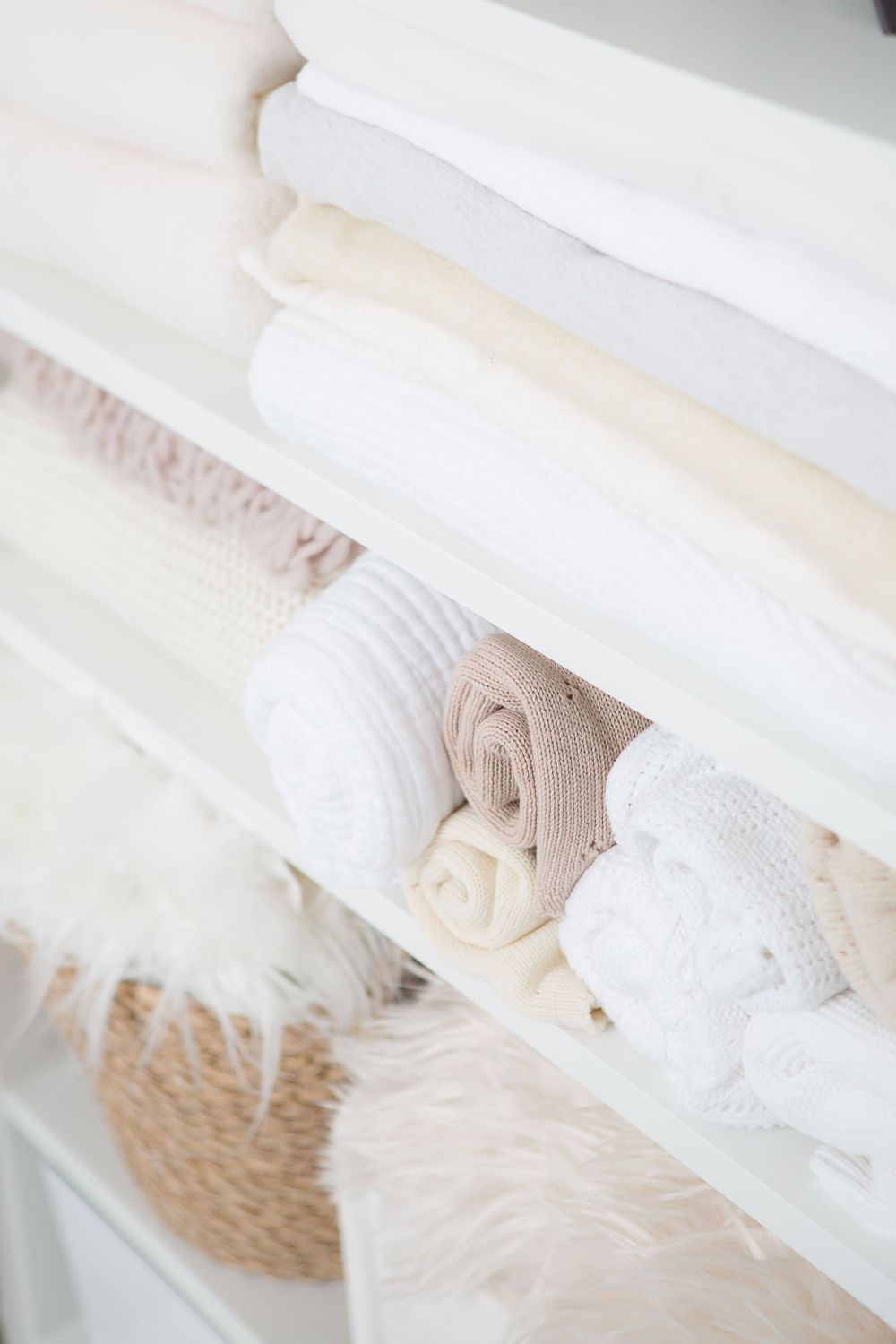 Neatly folded white and beige linens and towels stacked on shelves with a woven basket below.
